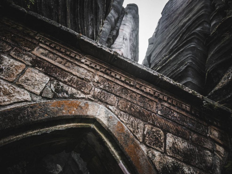A close-up of a weathered stone archway with intricate carvings, leading to towering rock formations