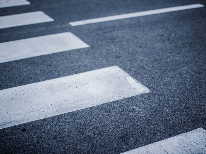 Close-up of a dark asphalt road with white painted crosswalk stripes, fading into the distance