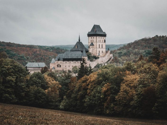 Karlštejn Castle in the Czech Republic, a large medieval fortress with dark roofs, surrounded by autumn trees