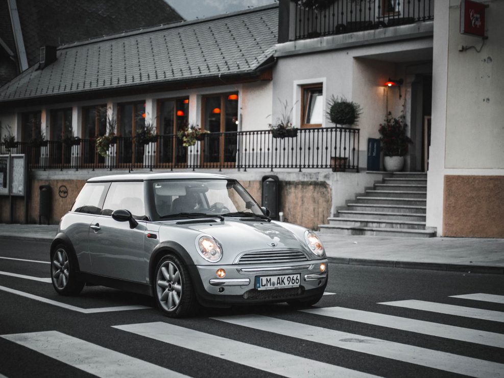 A silver Mini Cooper driving on a zebra crossing in a small Italian town