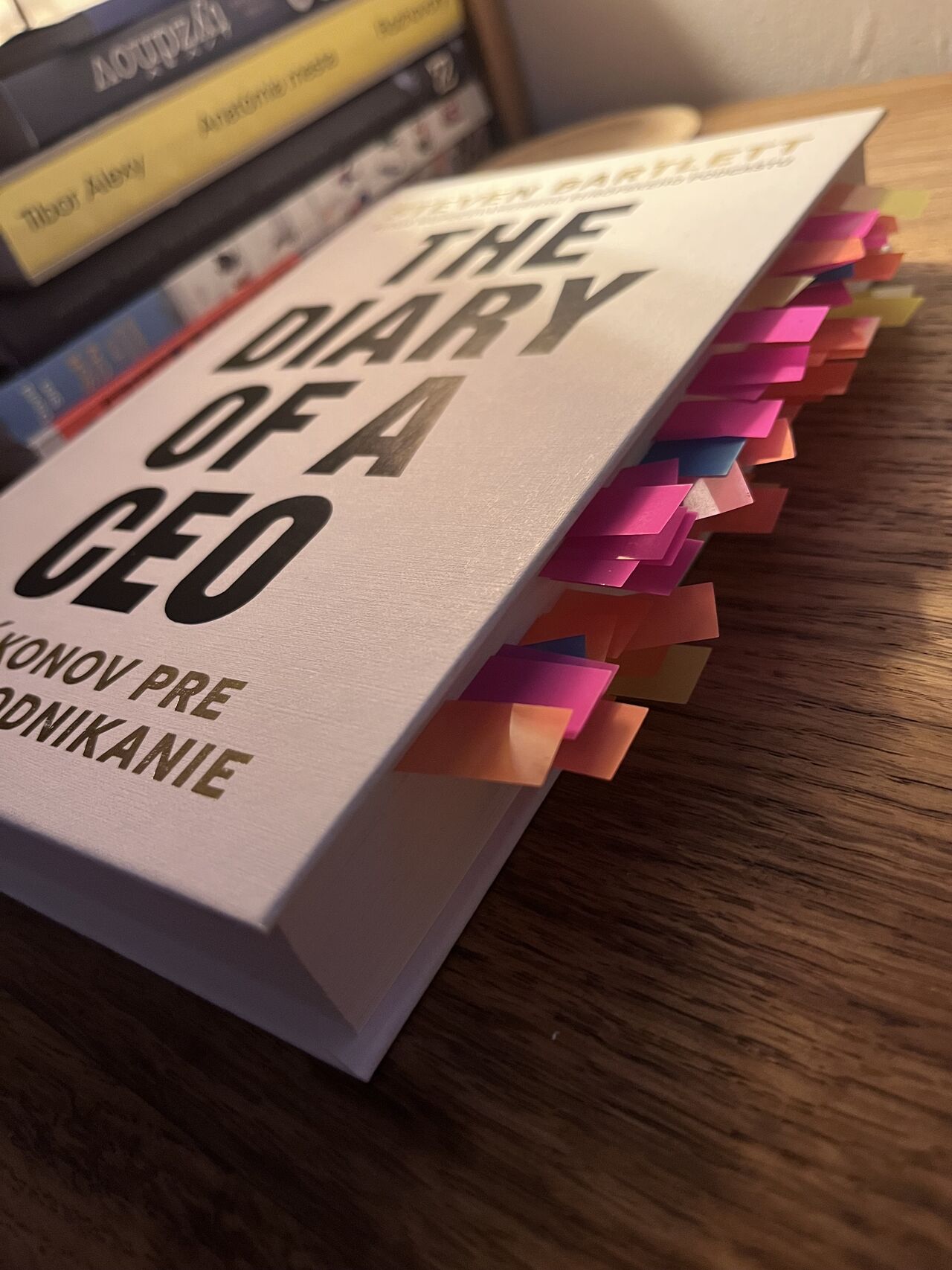 The Diary of a CEO by Steven Bartlett lying on a wooden table, its pages marked with dozens of pink, orange and blue sticky notes